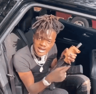 A Man With Dreadlocks Is Sitting In The Back Seat Of A Car Holding A Gun GIF