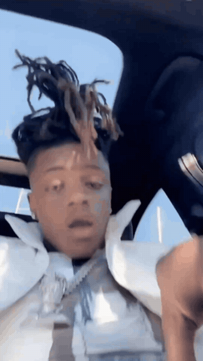 A Man With Dreadlocks Is Sitting In The Back Seat Of A Car With His Head In The Air . GIF