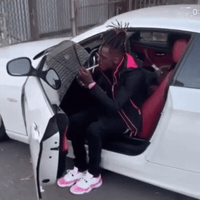 A Man With Dreadlocks Is Sitting In The Back Seat Of A White Car Smoking A Cigarette . GIF
