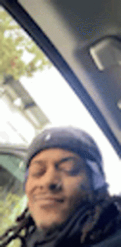 A Man With Dreadlocks Is Sitting In The Driver 'S Seat Of A Car And Smiling . GIF