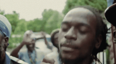 A Man With Dreadlocks Is Smoking A Cigarette In Front Of A Crowd Of People With Their Eyes Closed . GIF