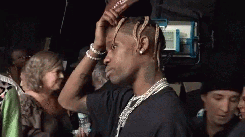 A Man With Dreadlocks Is Standing In A Crowd And Adjusting His Hair . GIF