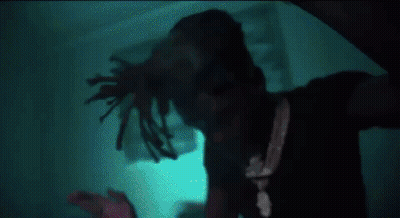 A Man With Dreadlocks Is Standing In A Dark Room In Front Of A Blue Light . GIF