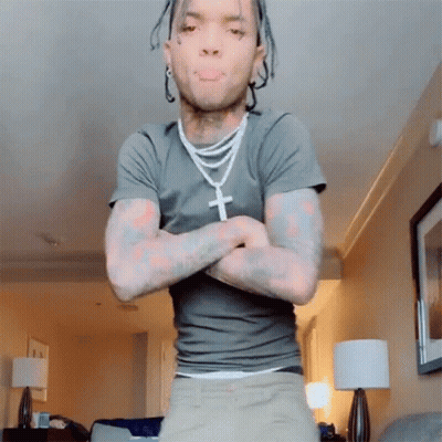 A Man With Dreadlocks Is Standing In A Living Room With His Arms Crossed GIF