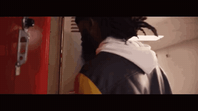 A Man With Dreadlocks Is Standing In Front Of A Red Locker In A Hallway . GIF
