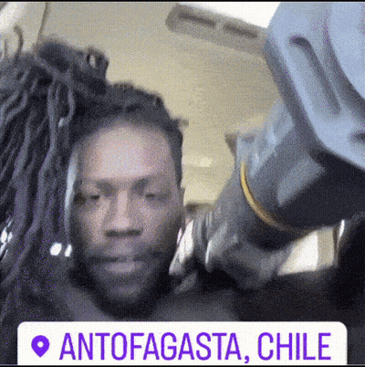 A Man With Dreadlocks Is Standing Next To Another Man With Dreadlocks And A Sign That Says Antofagasta Chile GIF
