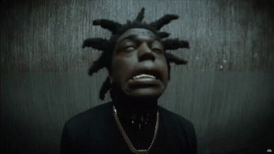A Man With Dreadlocks Is Wearing A Black Shirt And Gold Chain GIF