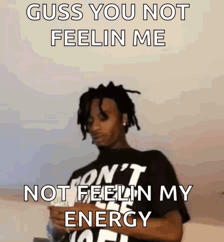 A Man With Dreadlocks Is Wearing A Black Shirt That Says ' Guss You Not Feelin Me ' On It . GIF