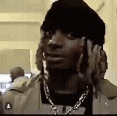 A Man With Dreadlocks Is Wearing A Hat And A Necklace . GIF