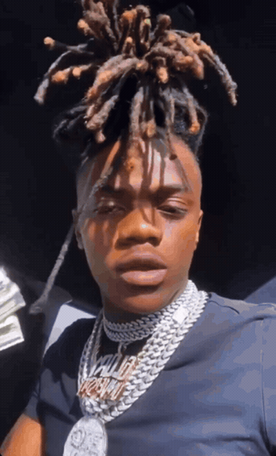 A Man With Dreadlocks Is Wearing A Necklace That Says ' King ' On It . GIF