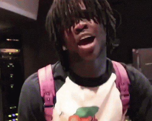 A Man With Dreadlocks Is Wearing A Pink Backpack And A White Shirt With A Peach On It . GIF