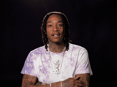 A Man With Dreadlocks Is Wearing A Purple Tie Dye Shirt And Necklaces GIF