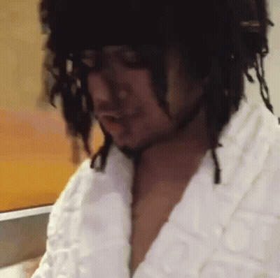 A Man With Dreadlocks Is Wearing A White Robe And A Black Hat . GIF