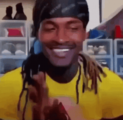 A Man With Dreadlocks Is Wearing A Yellow Shirt And A Black Headband And Smiling . GIF