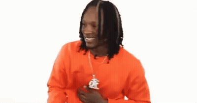 A Man With Dreadlocks Is Wearing An Orange Sweater And A Necklace With A Pendant . GIF