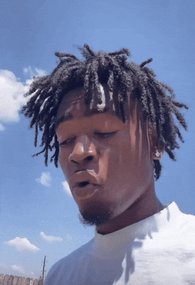 A Man With Dreadlocks Looks At The Camera With A Blue Sky Behind Him GIF