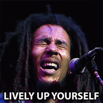 A Man With Dreadlocks Singing Into A Microphone With The Words Lively Up Yourself Behind Him GIF