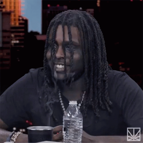 A Man With Dreadlocks Sits At A Table With A Bottle Of Water And A Cup GIF