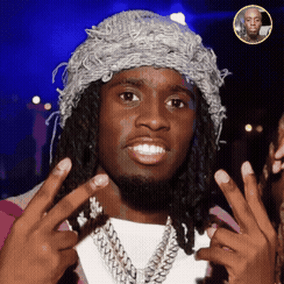 A Man With Dreadlocks Wearing A Hat And A Necklace Is Giving A Peace Sign GIF