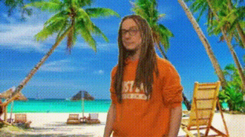 A Man With Dreadlocks Wearing An Orange Shirt With The Number 57 On It Stands On A Beach GIF