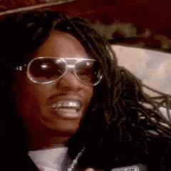 A Man With Dreadlocks Wearing Sunglasses And A Microphone Says How 'S GIF