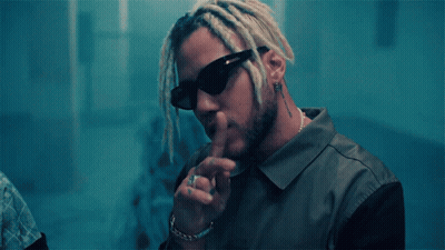 A Man With Dreadlocks Wearing Sunglasses Has His Finger On His Mouth GIF
