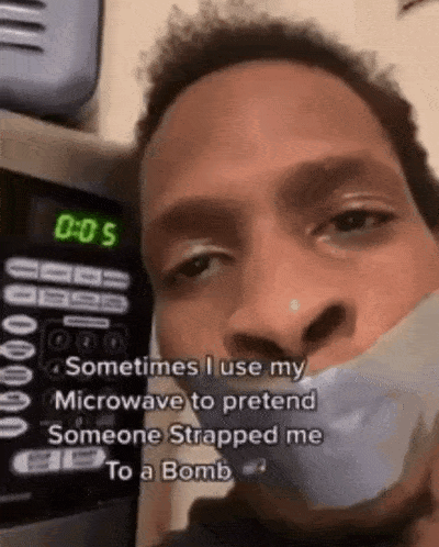 A Man With Duct Tape Around His Mouth Is Standing In Front Of A Microwave With The Time 0:05 On It . GIF