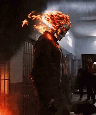A Man With Flames Coming Out Of His Head Is Standing In A Dark Room GIF