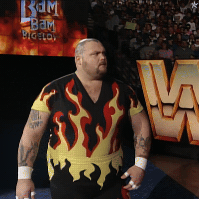 A Man With Flames On His Shirt Is Standing In Front Of A Sign That Says Bam Bigelow GIF