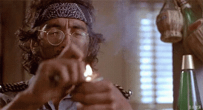 A Man With Glasses And A Bandana On His Head Is Lighting A Cigarette With A Lighter . GIF