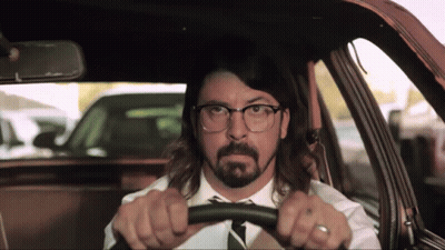 A Man With Glasses And A Beard Driving A Car GIF