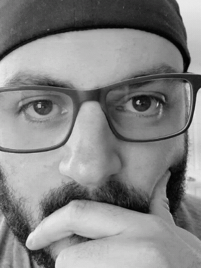 A Man With Glasses And A Beard Holds His Hand To His Face GIF