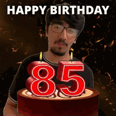 A Man With Glasses And A Beard Is Holding A Birthday Cake With Candles In The Shape Of The Number 85 GIF