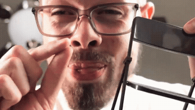A Man With Glasses And A Beard Is Holding A Black Object In Front Of His Face GIF