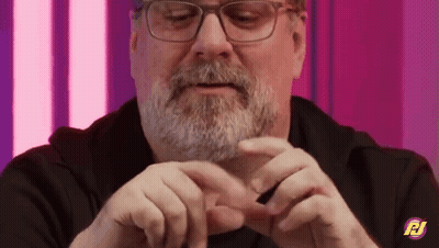 A Man With Glasses And A Beard Is Holding Something In His Hands And Making A Heart Shape With His Hands . GIF