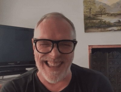 A Man With Glasses And A Beard Is Laughing In Front Of A Panasonic Television GIF