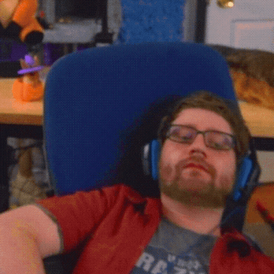 A Man With Glasses And A Beard Is Laying In A Chair With His Arm Up In The Air GIF