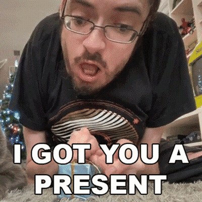 A Man With Glasses And A Beard Is Laying On The Floor And Says I Got You A Present In White GIF