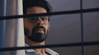 A Man With Glasses And A Beard Is Peeking Out Of A Window . GIF