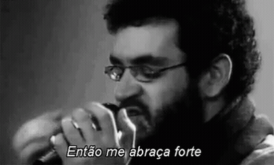 A Man With Glasses And A Beard Is Singing Into A Microphone . GIF