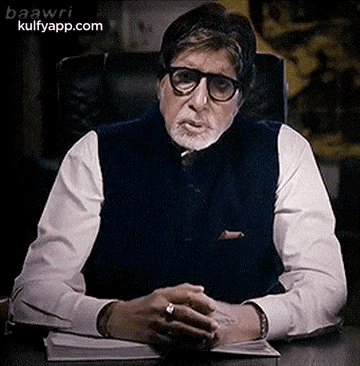 A Man With Glasses And A Beard Is Sitting At A Desk . GIF