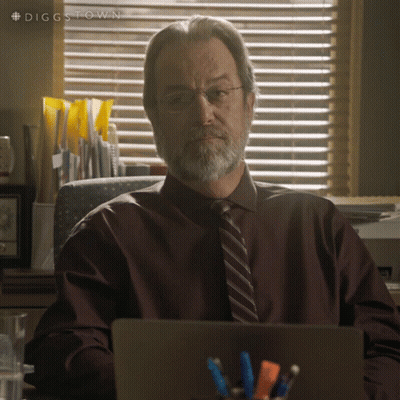 A Man With Glasses And A Beard Is Sitting At A Desk With A Laptop In Front Of Him GIF