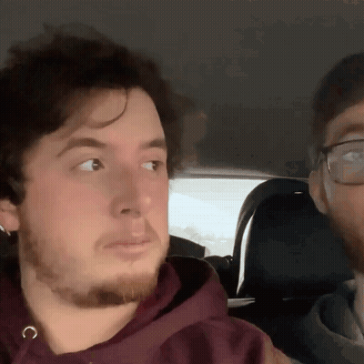 A Man With Glasses And A Beard Is Sitting In A Car With Another Man GIF
