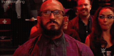 A Man With Glasses And A Beard Is Sitting In A Crowd With A Sign That Says Neville . GIF