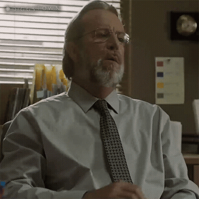 A Man With Glasses And A Beard Is Sitting In Front Of A Window With A Sign That Says #Diggstown On It GIF