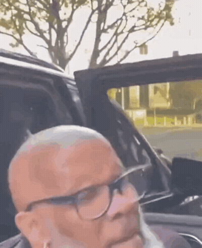 A Man With Glasses And A Beard Is Sitting In The Back Seat Of A Car . GIF