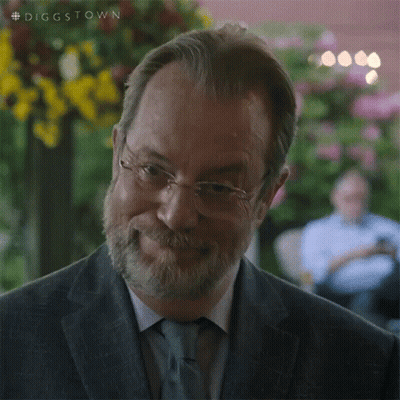 A Man With Glasses And A Beard Is Smiling And Looking At The Camera . GIF