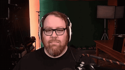 A Man With Glasses And A Beard Is Wearing Headphones In Front Of A Green Screen GIF