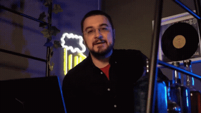 A Man With Glasses And A Beard Says " Scappa " In Front Of A Neon Sign GIF