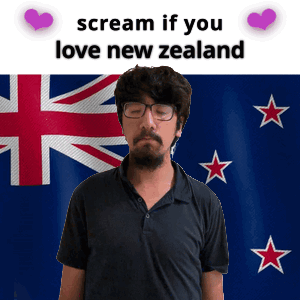 A Man With Glasses And A Beard Stands In Front Of A New Zealand Flag GIF